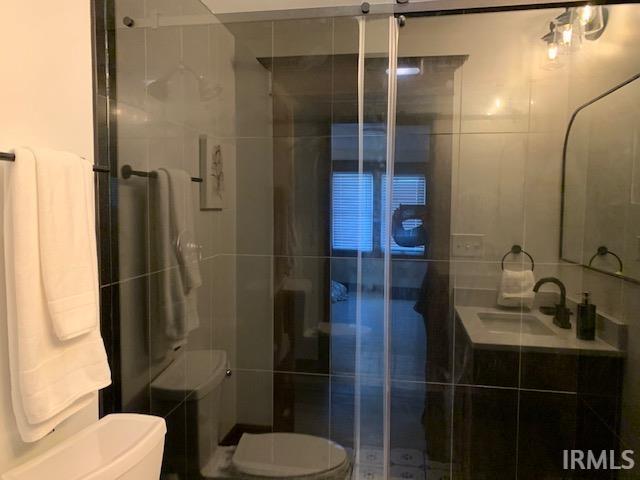 full bathroom featuring a stall shower, toilet, tile walls, and a sink