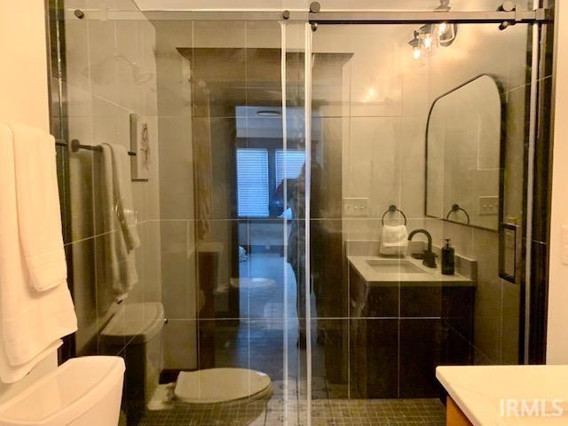 bathroom featuring vanity, tile walls, toilet, and a shower stall