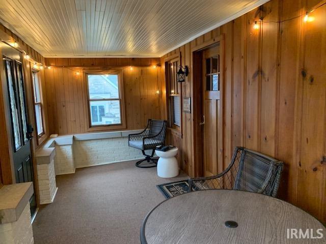 living area featuring wood walls, wooden ceiling, and carpet floors