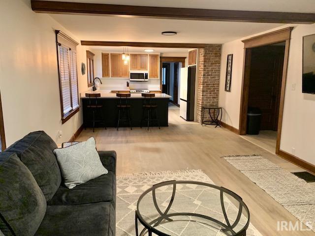 living room featuring light wood finished floors, beamed ceiling, and baseboards