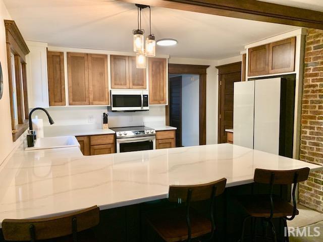 kitchen featuring appliances with stainless steel finishes, brick wall, light countertops, and a peninsula