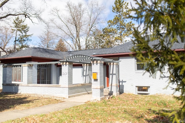 view of front of house featuring brick siding, a front lawn, and roof with shingles