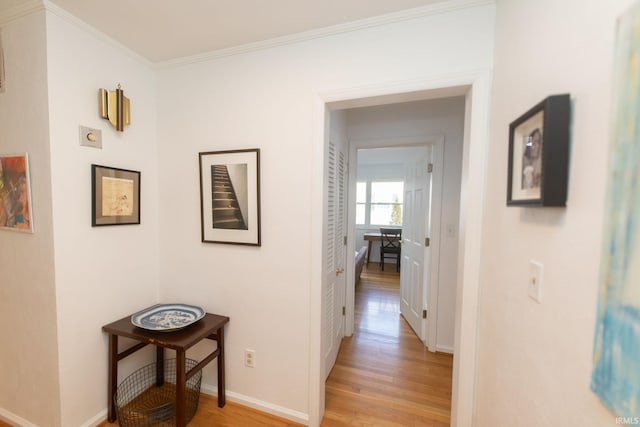 hallway with light wood-style floors, baseboards, and ornamental molding