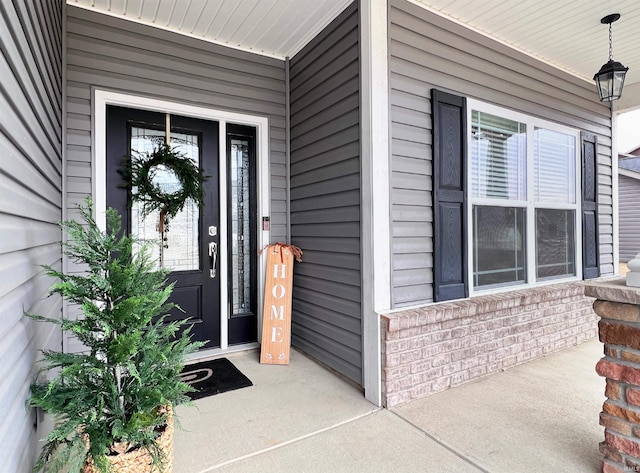 doorway to property with a porch and brick siding