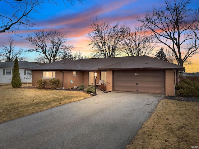 view of front facade featuring a garage, driveway, brick siding, and a lawn