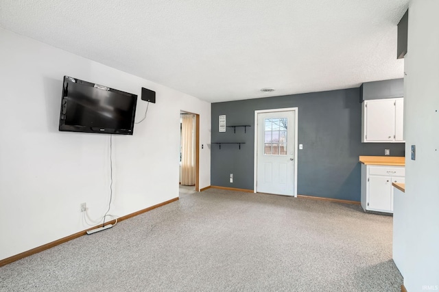 unfurnished living room with light carpet, baseboards, and a textured ceiling