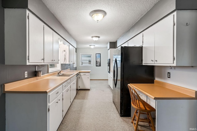 kitchen featuring white cabinetry, light countertops, a textured ceiling, and freestanding refrigerator