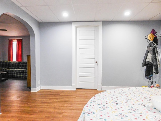 bedroom featuring light wood finished floors, baseboards, arched walkways, and a drop ceiling