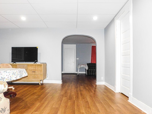 bedroom featuring arched walkways, a drop ceiling, baseboards, and wood finished floors