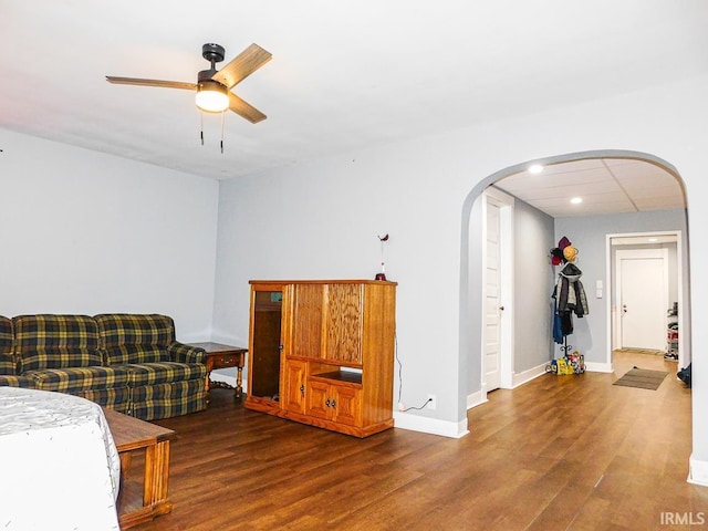 living room with arched walkways, wood finished floors, a ceiling fan, and baseboards