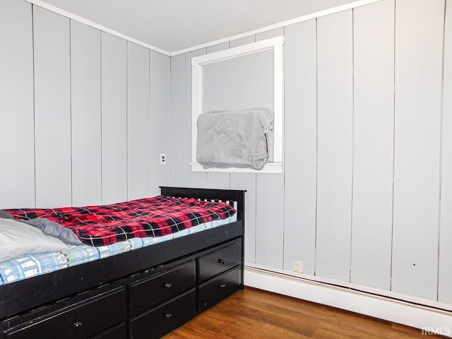 bedroom with a baseboard heating unit and dark wood finished floors