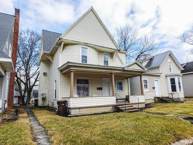 victorian home with a porch, a front yard, and a shingled roof