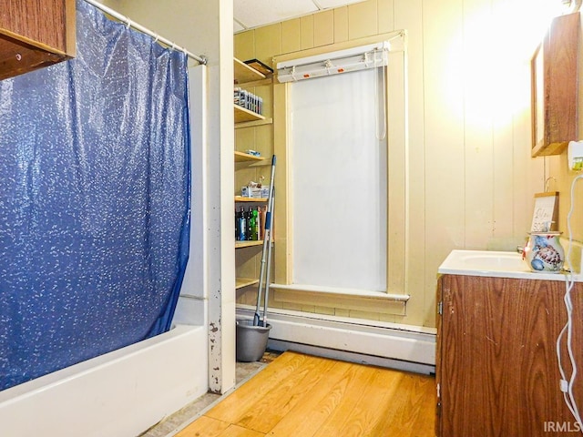 full bathroom featuring a baseboard radiator, shower / bathtub combination with curtain, wooden walls, vanity, and wood finished floors