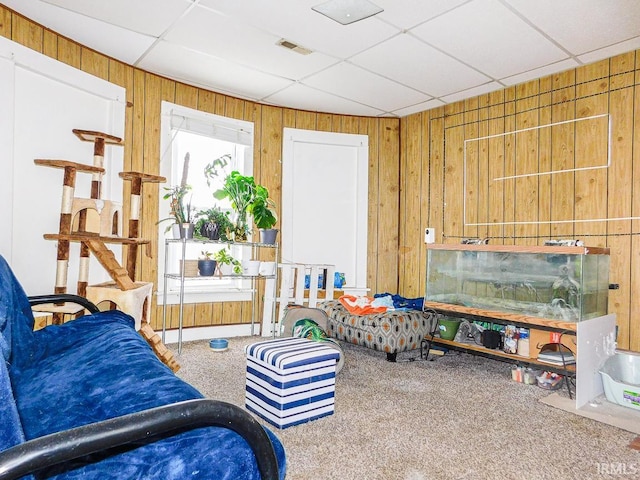 sitting room with wood walls, a drop ceiling, carpet flooring, and visible vents