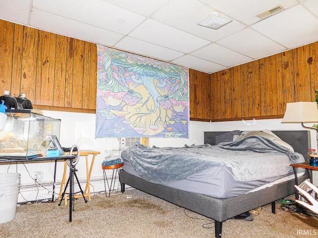 carpeted bedroom featuring wooden walls, visible vents, and a drop ceiling