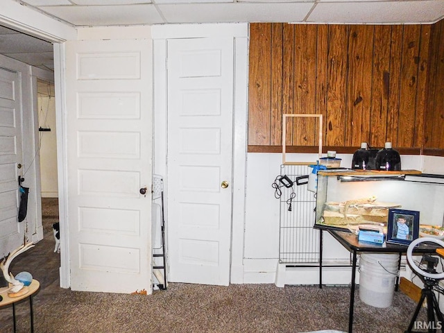 misc room featuring a drop ceiling, carpet flooring, and wooden walls