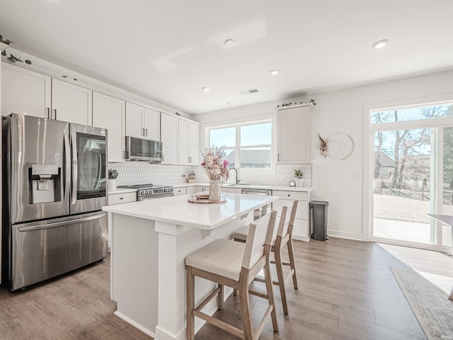 kitchen with light wood-style flooring, a kitchen breakfast bar, light countertops, appliances with stainless steel finishes, and tasteful backsplash