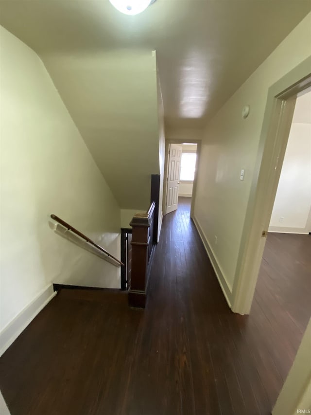 corridor with vaulted ceiling, baseboards, dark wood finished floors, and an upstairs landing