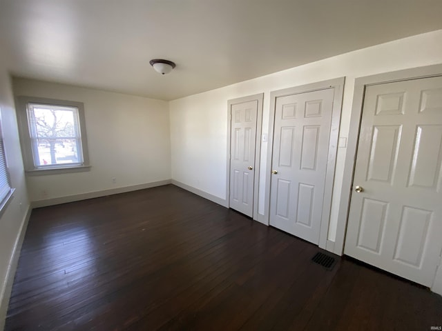 unfurnished bedroom with visible vents, dark wood finished floors, and baseboards