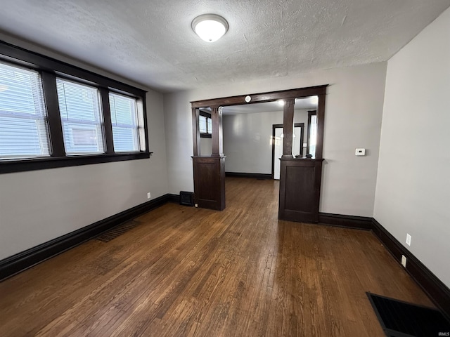 empty room featuring a textured ceiling, dark wood finished floors, visible vents, and baseboards