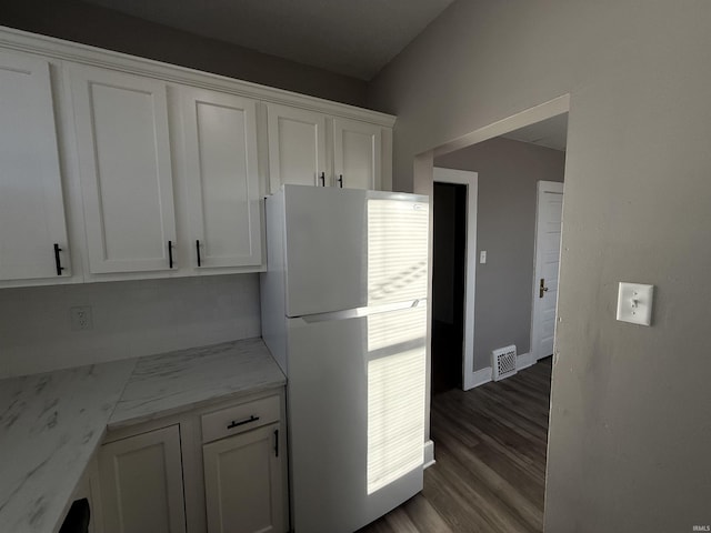 kitchen featuring dark wood-style floors, white cabinetry, light stone counters, and freestanding refrigerator