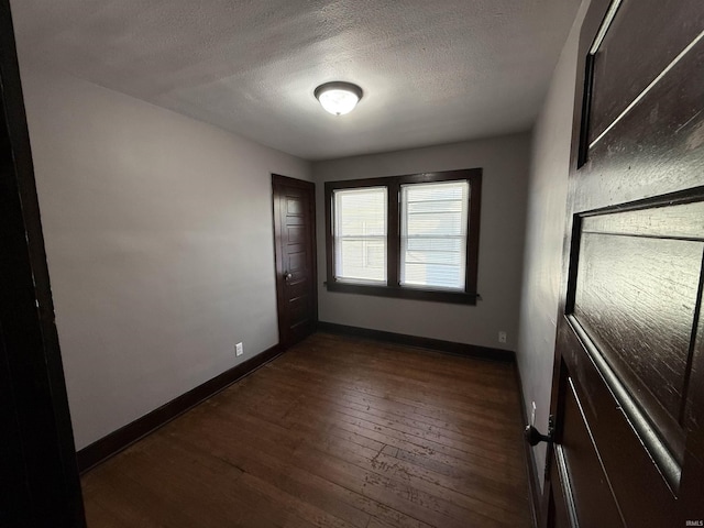 spare room with baseboards, dark wood finished floors, and a textured ceiling