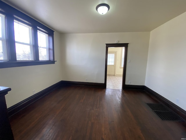 spare room with baseboards, visible vents, and dark wood-style flooring