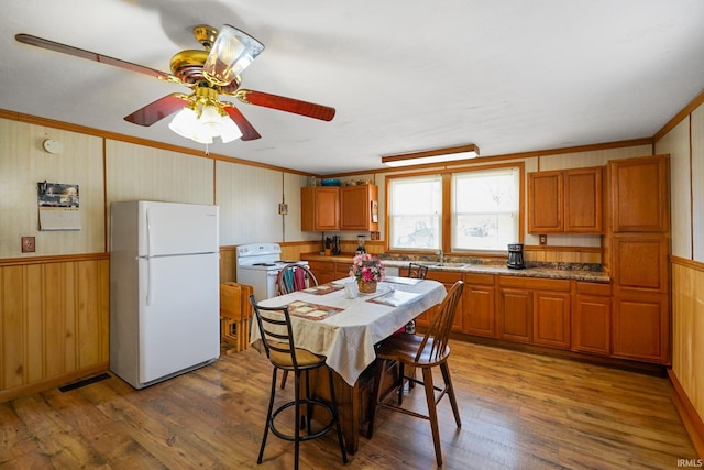 kitchen featuring brown cabinetry, wood finished floors, freestanding refrigerator, and crown molding