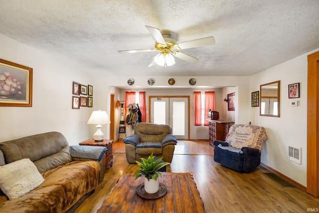 living room with a textured ceiling, visible vents, wood finished floors, and french doors