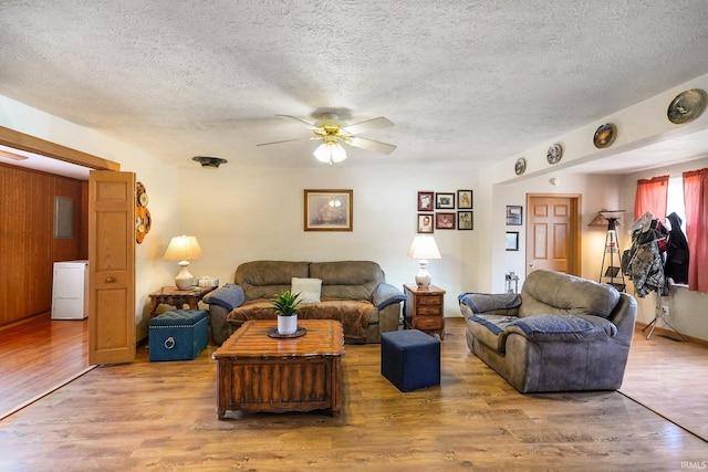 living room featuring a textured ceiling, wood walls, wood finished floors, and a ceiling fan