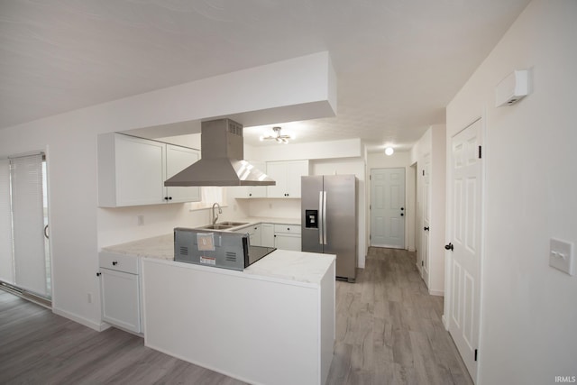 kitchen featuring island exhaust hood, light wood-style flooring, white cabinets, a sink, and stainless steel fridge