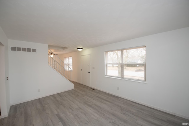 unfurnished living room with wood finished floors, visible vents, baseboards, and stairs