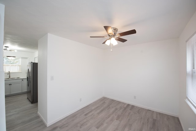 spare room featuring light wood-type flooring, a sink, baseboards, and ceiling fan