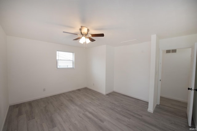 empty room featuring a ceiling fan, visible vents, baseboards, and wood finished floors