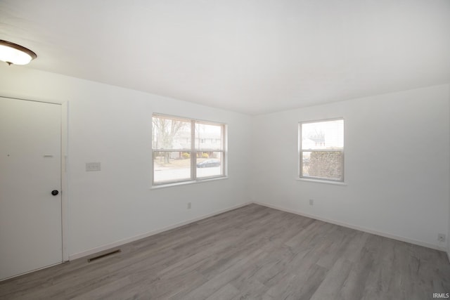 spare room with baseboards, plenty of natural light, visible vents, and light wood-style floors