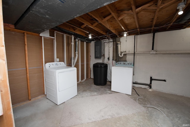 unfinished below grade area featuring concrete block wall, electric panel, and washing machine and clothes dryer