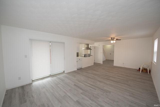 unfurnished living room featuring a textured ceiling, baseboards, light wood-style flooring, and a ceiling fan