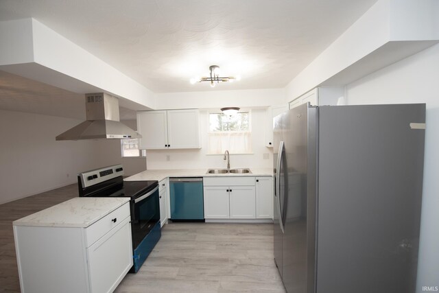 kitchen featuring stainless steel appliances, light wood-style floors, white cabinets, a sink, and wall chimney range hood