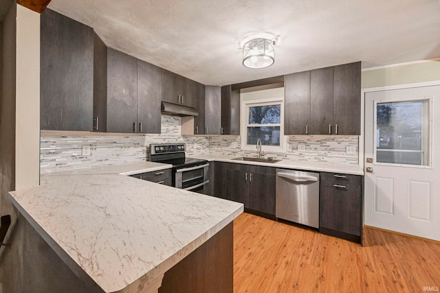 kitchen featuring stainless steel appliances, light countertops, a sink, a peninsula, and under cabinet range hood