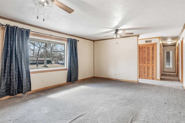 carpeted empty room with baseboards, ornamental molding, visible vents, and a ceiling fan