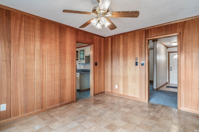 spare room featuring wood walls, a ceiling fan, and crown molding