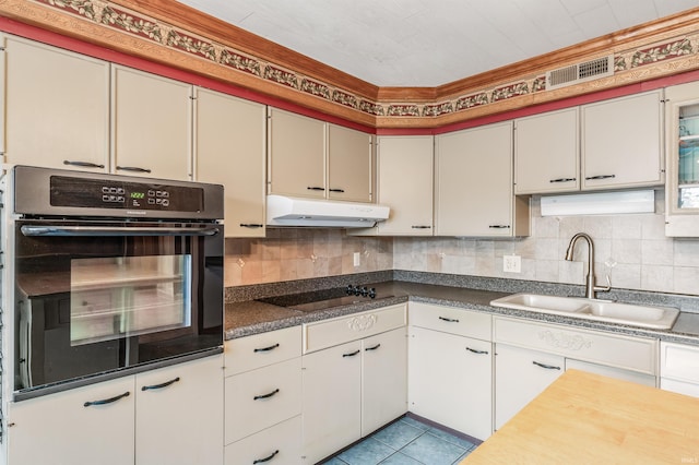 kitchen with black appliances, tasteful backsplash, under cabinet range hood, and a sink