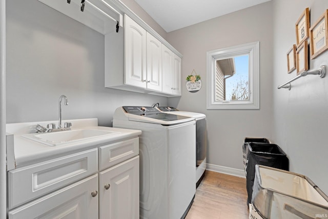 laundry room with a sink, baseboards, light wood-style floors, washer and dryer, and cabinet space