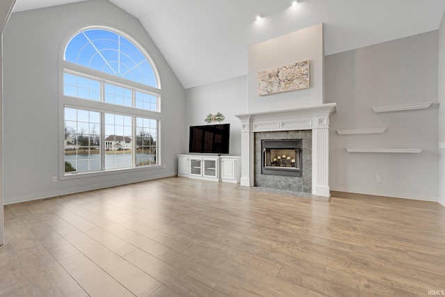 unfurnished living room featuring high vaulted ceiling, a tiled fireplace, wood finished floors, and baseboards