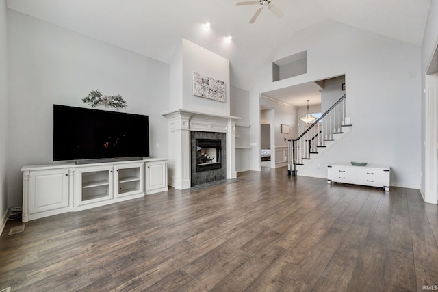 unfurnished living room featuring ceiling fan, high vaulted ceiling, dark wood-style flooring, a fireplace, and stairs