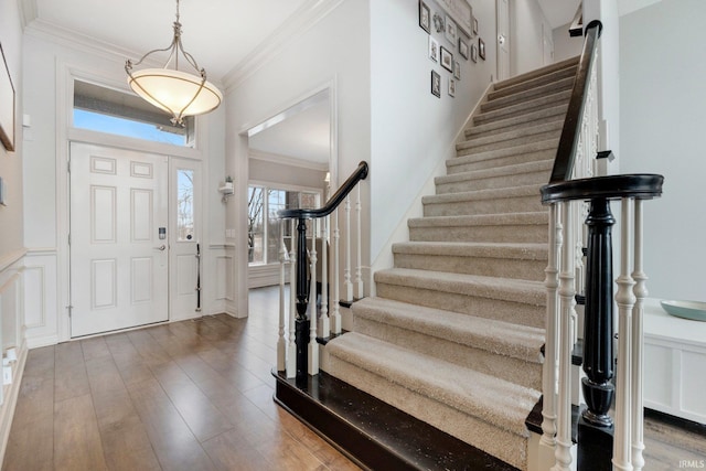 entrance foyer with ornamental molding, wainscoting, wood finished floors, and a decorative wall