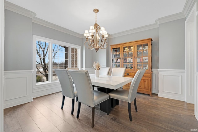 dining area featuring a wainscoted wall, ornamental molding, a notable chandelier, and wood finished floors