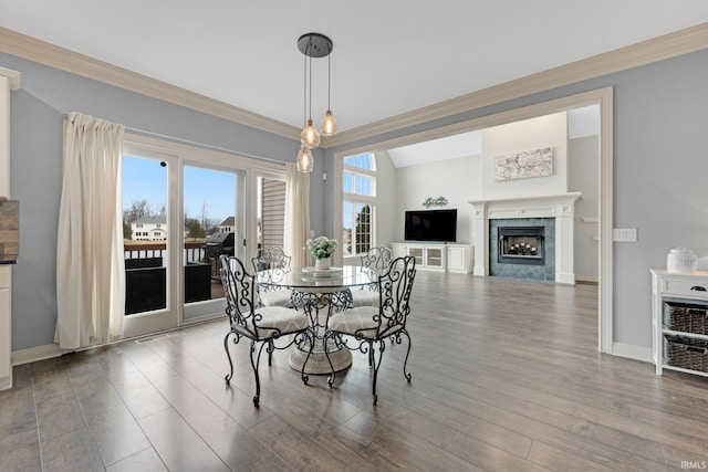 dining space with a fireplace, crown molding, baseboards, and wood finished floors