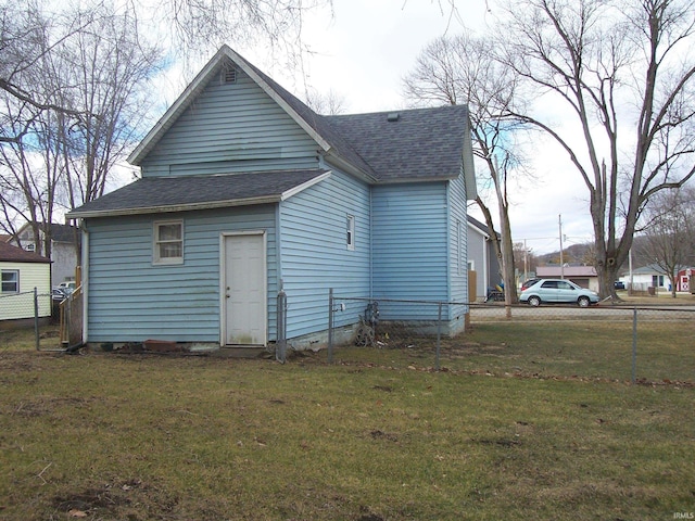 rear view of property featuring a shingled roof, fence, and a yard