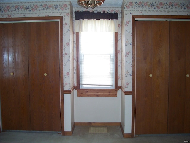 unfurnished bedroom with wallpapered walls, visible vents, multiple windows, and baseboards